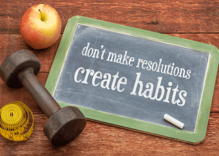 Chalkboard says "don't make resolutions, create habits" alongside an apple, dumbbell, and tape measure.