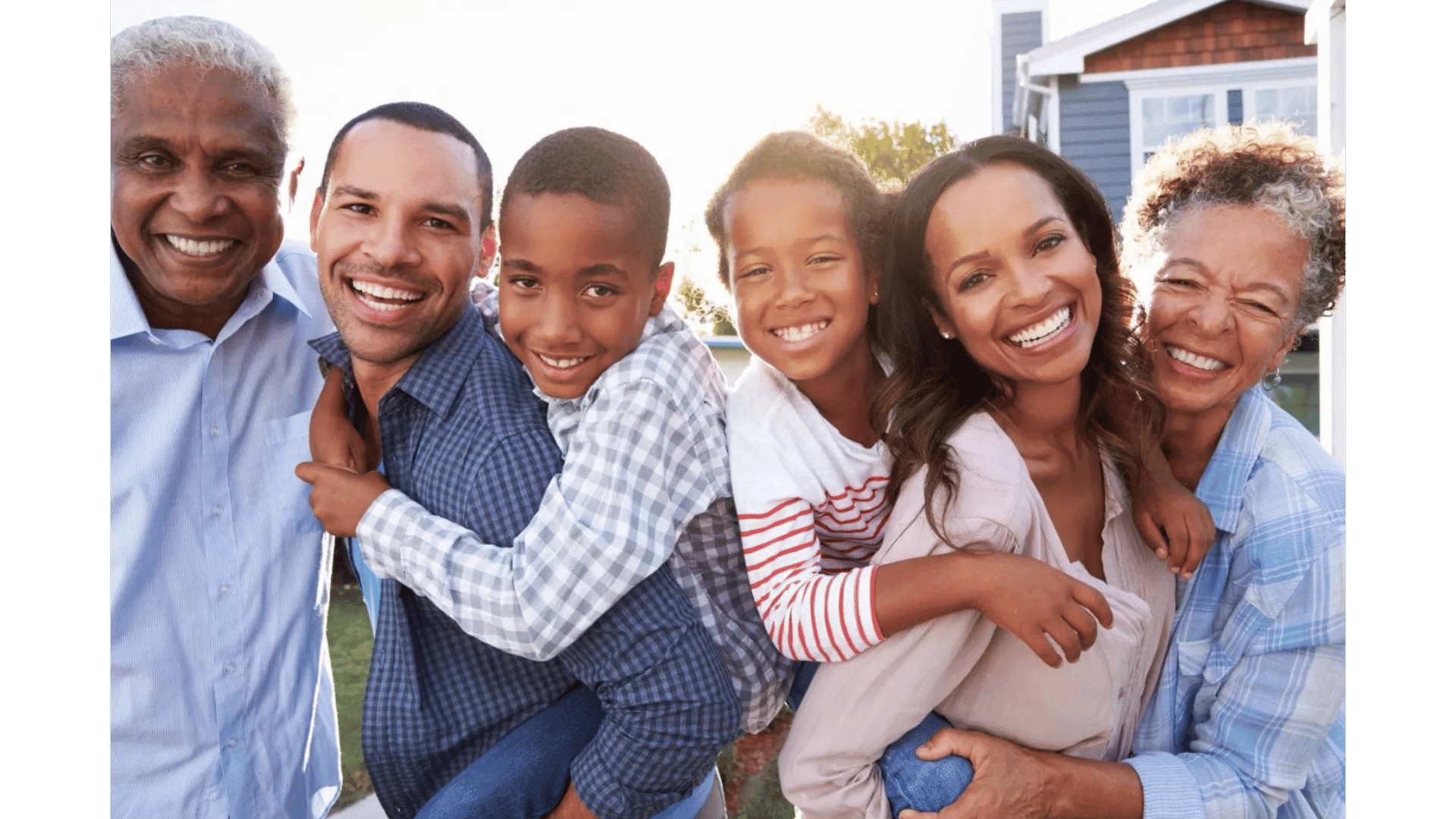 Family of six smiling and posing together in front of a house on a sunny day.